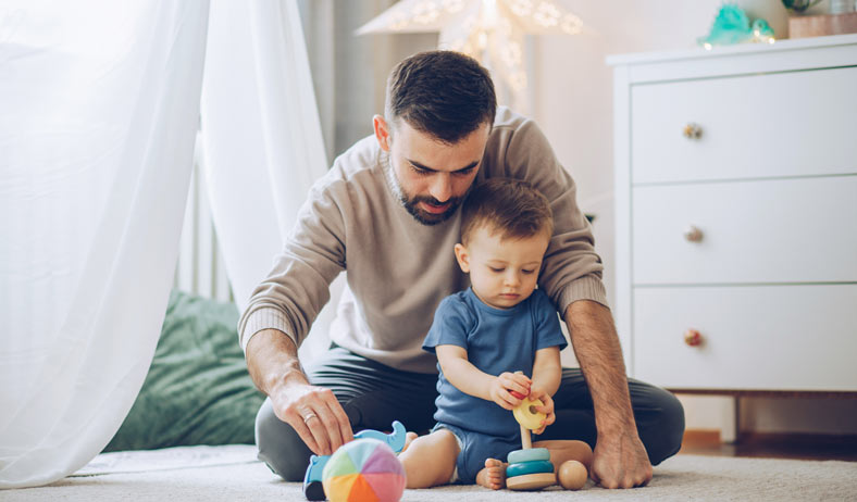 Dad and toddler playing with stacking toys on the floor together